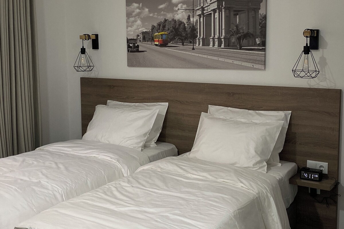 A hotel room with a double bed, a headboard, a wall-mounted picture, two bedside tables with lamps, and a carpeted floor.