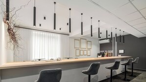 Un espace bar moderne avec un comptoir en bois, des tabourets de bar, des luminaires suspendus et des tableaux encadrés au mur.