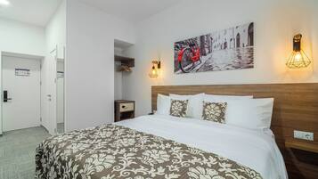 A hotel room with a bed, a nightstand, a wall-mounted light, and a door.