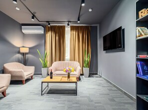 A modern living room with a beige sofa, a coffee table with a vase of flowers, a floor lamp, and a bookshelf with books and a TV.