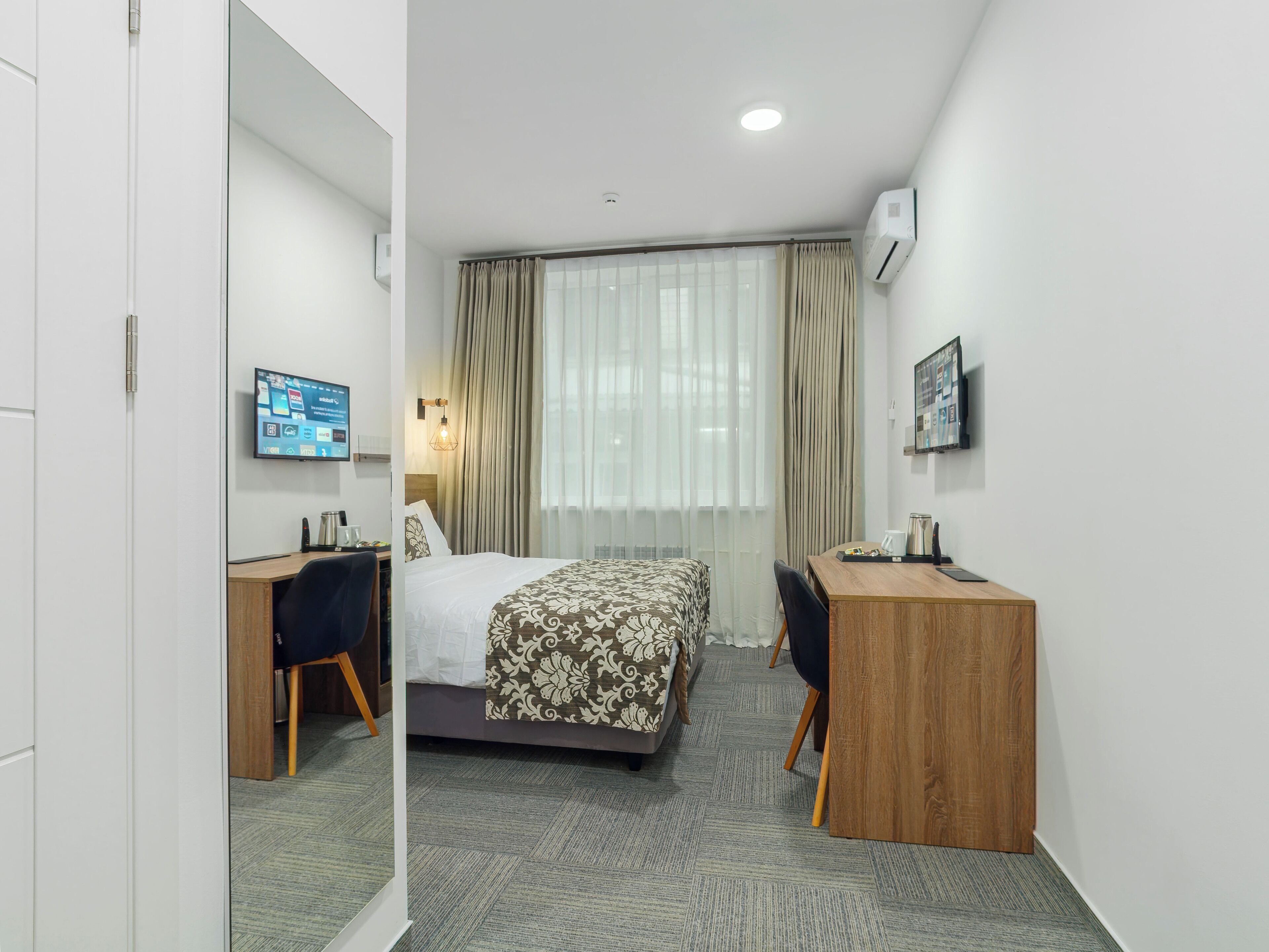 Habitación de hotel con cama, escritorio, silla, televisión y ventana con cortinas.