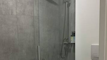 Een moderne badkamer met een douchecabine, toilet en een wandmengkraan.