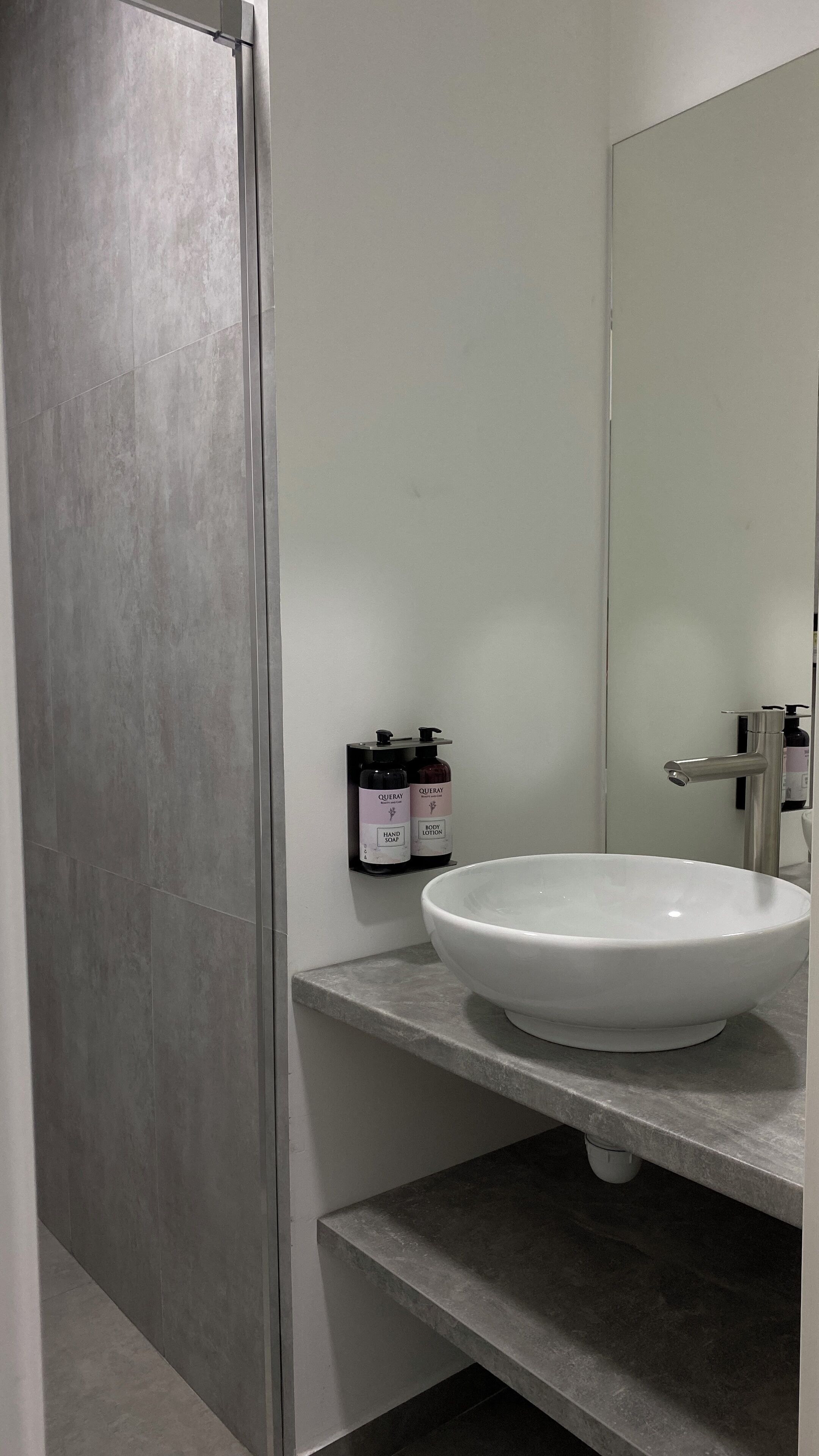 A bathroom with a white sink, a mirror, and two bottles of hand soap and body lotion on a shelf.