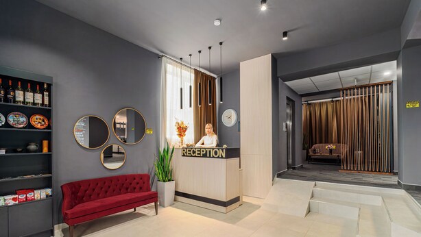 Un espace d’accueil avec un canapé rouge, un comptoir de réception et un mur orné de miroirs ronds.