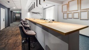 Un espace bar moderne avec un long comptoir en bois, de nombreux tabourets de bar, des luminaires suspendus et des tableaux encadrés au mur.