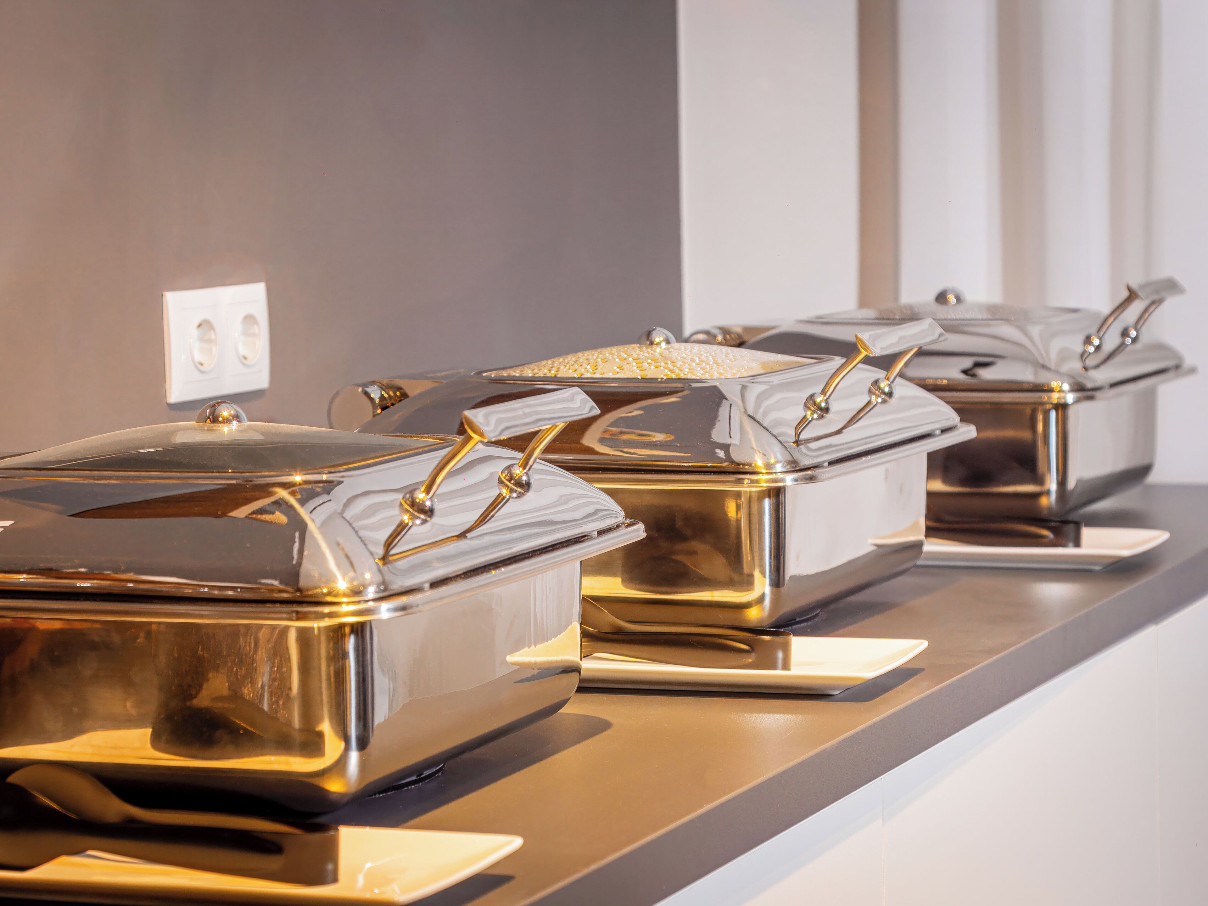 A row of stainless steel food service containers with gold handles on a countertop.