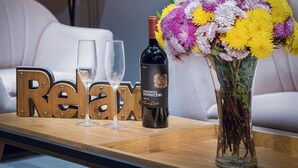 Une table en bois sur laquelle reposent deux verres à vin vides, une bouteille de Doménil-Viniceni et un vase rempli de fleurs aux couleurs vives.