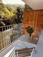 A balcony with a wooden table, a vase with flowers, and a view of a forested area.