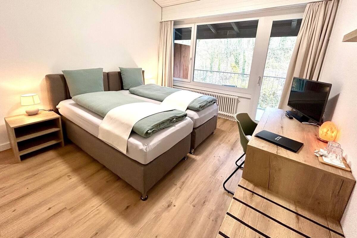 A modern bedroom with a bed, bedside tables, a desk, and a television.