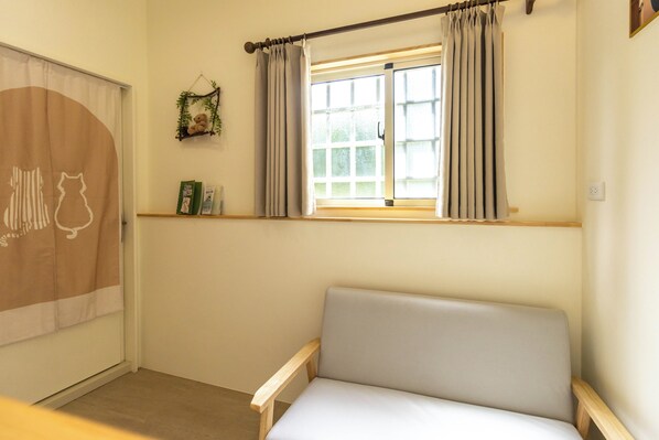A room with a beige sofa, a window with curtains, a wall-mounted shelf with books, and a decorative item above the window. - TurnLeftHome (Wujie)