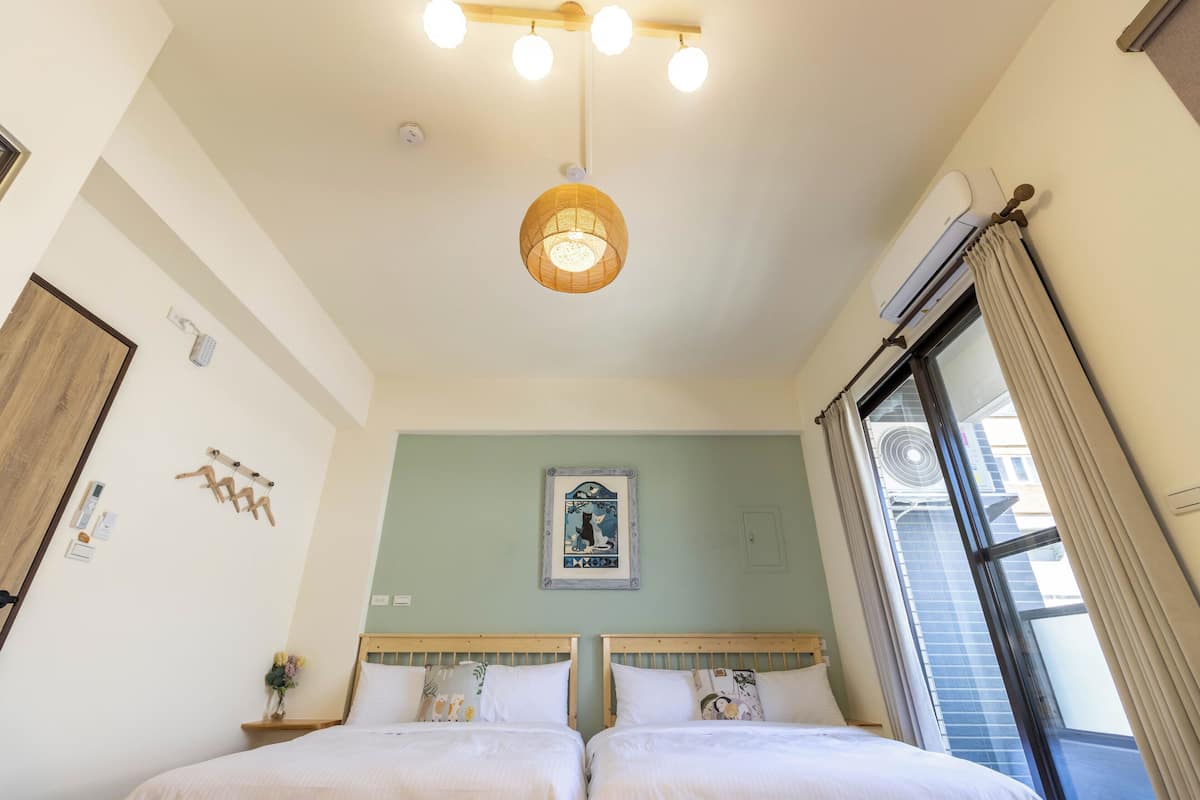 A bedroom with two beds, a hanging light fixture, a wall-mounted air conditioner, and a window with curtains.