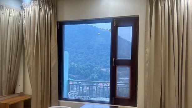 Habitación de hotel con una cama, una mesa y dos sillas, una ventana con cortinas y vistas a un paisaje montañoso.