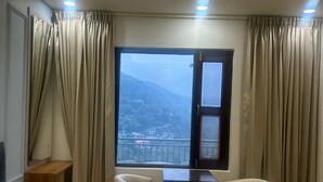 Habitación de hotel con cama, escritorio, dos sillas y ventana con vista a la montaña, además de cortinas.