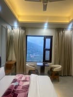 Habitación de hotel con cama, escritorio, dos sillas y ventana con vista a la montaña, además de cortinas.