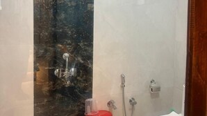 Un baño con pared de mármol, ducha e inodoro.