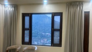Una habitación con dos sillas de madera, una cama con colcha estampada, un ventanal con cortinas y vistas a un paisaje montañoso.