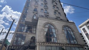 Un grand immeuble doté de nombreuses fenêtres, une entrée centrale avec un escalier, et un ciel dégagé.