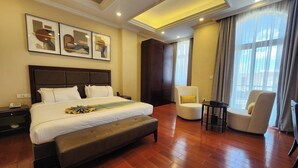 Une chambre d’hôtel avec un grand lit, une table de chevet avec un téléphone, une chaise, une petite table et une fenêtre avec des rideaux.