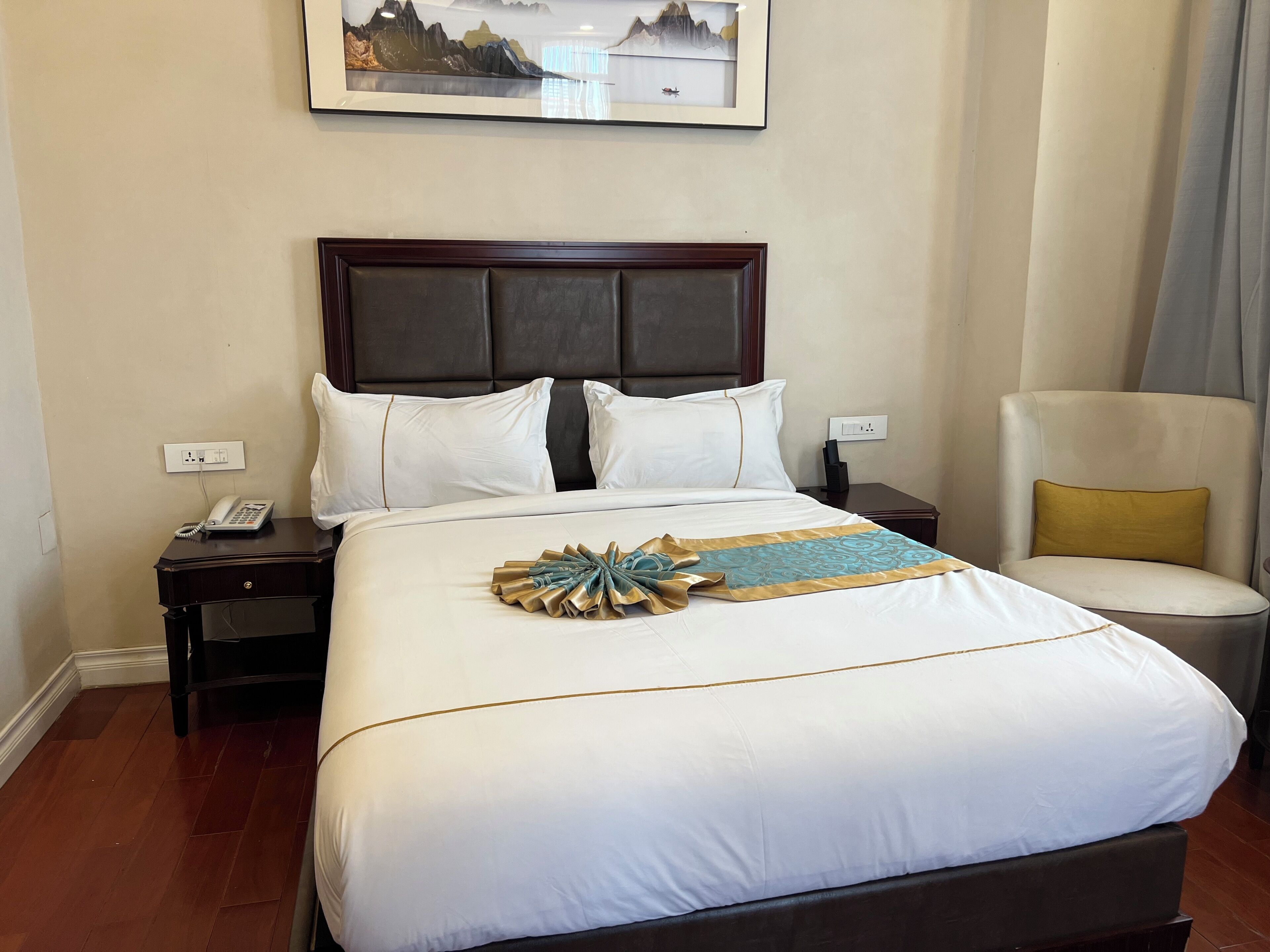 Habitación de hotel con una cama grande, una silla, una mesita de noche con teléfono y un cuadro colgado en la pared.