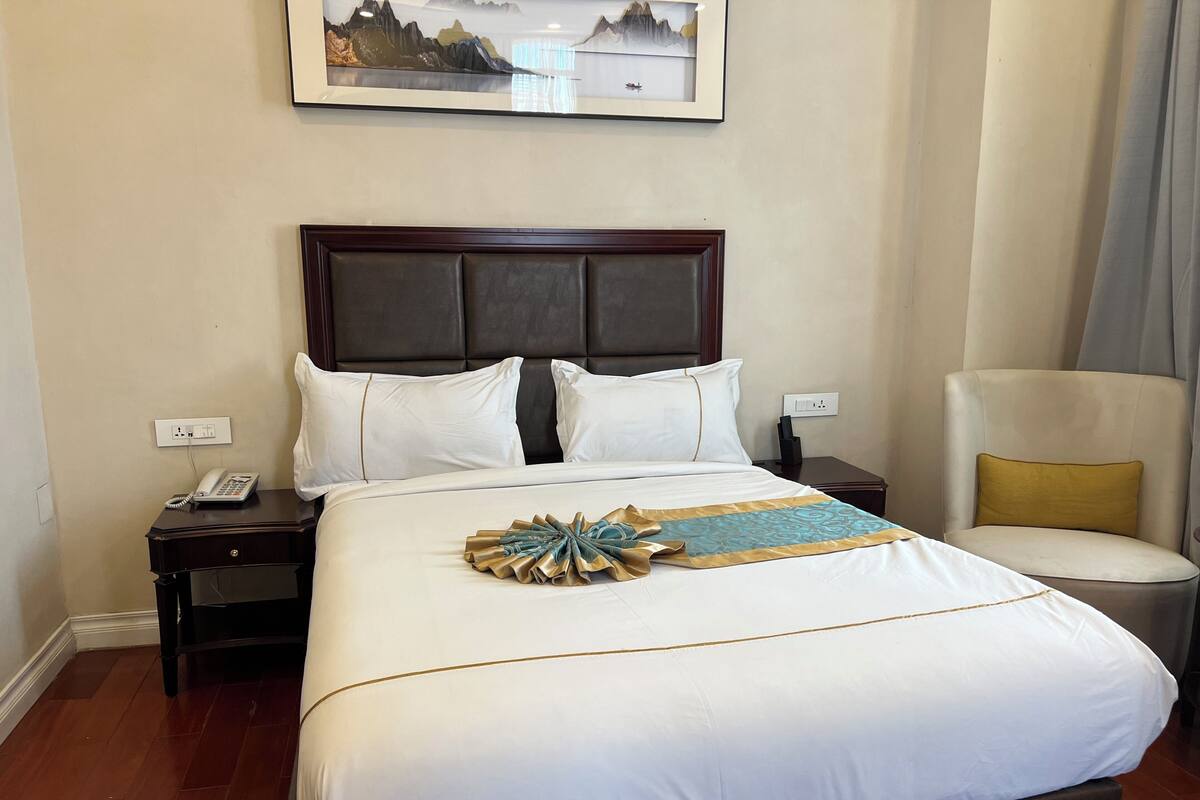 Une chambre d’hôtel avec un grand lit, une chaise, une table de chevet avec un téléphone et un tableau accroché au mur.
