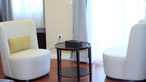 Une pièce avec deux fauteuils blancs, dont l’un est agrémenté d’un coussin jaune, et une petite table ronde sur laquelle se trouve une boîte.