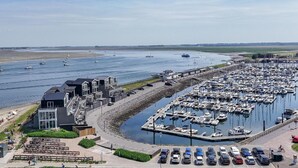 Un port de plaisance où sont amarrés de nombreux bateaux, une plage animée et un bâtiment à l’architecture moderne.