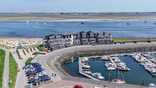 Un port de plaisance avec des bateaux amarrés, un parking et une plage où se trouvent des gens.