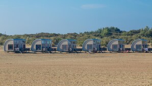 A row of beachside cabanas with a sandy beach and dunes in the background. - Appartement Bed by Al - Hoofdstraat 16 a Kortgene (Kortgene)