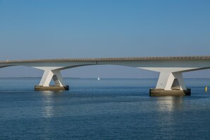 A bridge with a white structure spanning over water, with a sailboat visible in the distance. - Appartement Bed by Al - Hoofdstraat 16 a Kortgene (Kortgene)