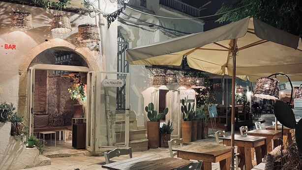 Um café ao ar livre com mesas e cadeiras de madeira, um poste de luz e plantas em vasos.