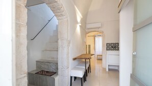 Um corredor com um arco de pedra, um banco de madeira, um banco de mármore, uma parede revestida de azulejos e uma porta branca.