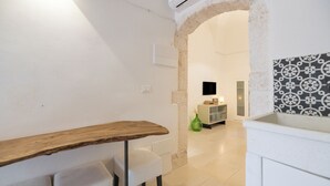 Interior moderno com mesa de madeira, cadeiras brancas, arco de pedra, TV e parede estampada.