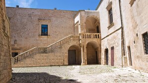 Pátio com edifícios de pedra, escadas e portas em arco.