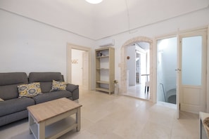 A living room with a sofa, a coffee table, a bookshelf, and an open door leading to another room. - Historic Home with Large Rooftop Terrace in Heart of Ceglie (Ceglie Messapica)