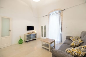 A living room with a sofa, a coffee table, a TV, a cabinet, and a green vase. - Historic Home with Large Rooftop Terrace in Heart of Ceglie (Ceglie Messapica)