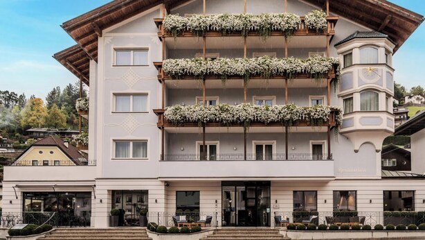 A multi-story hotel with balconies adorned with flowers, a restaurant on the ground floor, and a distinctive corner tower. - HOTIDAY Room Collection - Ortisei (Ortisei)