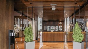 A hotel reception area with a wooden reception desk, glass doors, and two potted plants. - HOTIDAY Room Collection - Ortisei (Ortisei)