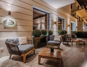 An outdoor seating area with wicker chairs and a wooden table, a glass sign with stars, and a building entrance. - HOTIDAY Room Collection - Ortisei (Ortisei)