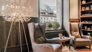 A room with leather chairs, a floor lamp, a window with a view of buildings and mountains, and a bookshelf. - HOTIDAY Room Collection - Ortisei (Ortisei)
