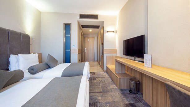 A hotel room with two beds, a TV, a desk, and a trash can. - Baskent Center Hotel (Ankara)