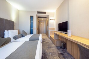 Une chambre d’hôtel avec deux lits, une télévision, un bureau et une poubelle.