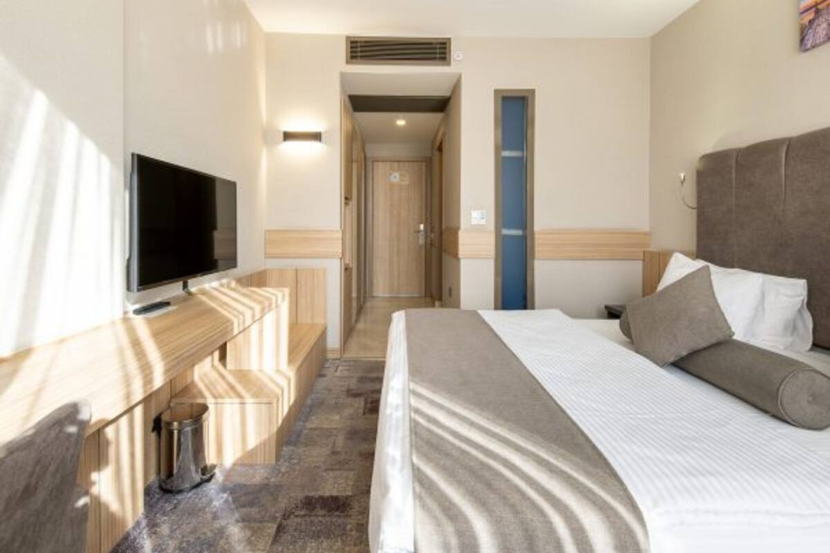 A hotel room with a bed, a TV, a desk, and a bathroom door.
