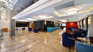 A modern lobby with marble flooring, blue seating, a reception desk, and a red wall with a Wi-Fi symbol. - Baskent Center Hotel (Ankara)