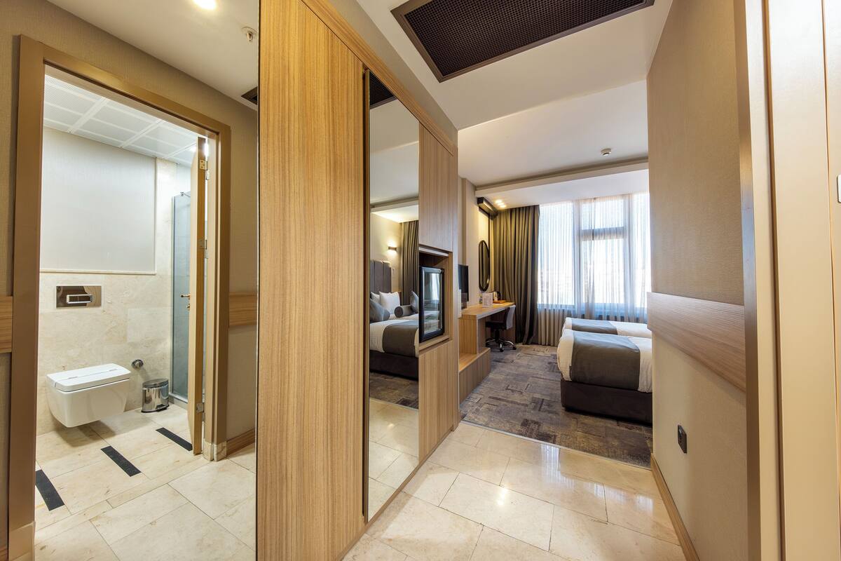 A modern hotel room with a bathroom, a desk, a bed, and a television.