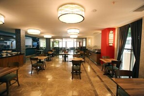 Ein geräumiges Restaurant mit mehreren Tischen und Stühlen, einem Küchenbereich und großen Fenstern, die für viel Tageslicht sorgen.