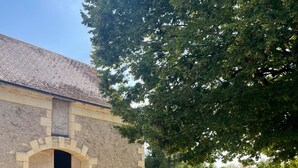 A stone building with a large arched doorway, surrounded by trees and a gravel path. - Chamber for young farmers  (Benais)