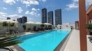 A swimming pool with lounge chairs and umbrellas, surrounded by tall buildings. - Czechin - Luma 22 (Dubai)