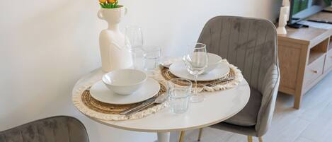 A dining table set with white plates, bowls, and glasses, a vase with yellow flowers, and a white pitcher.