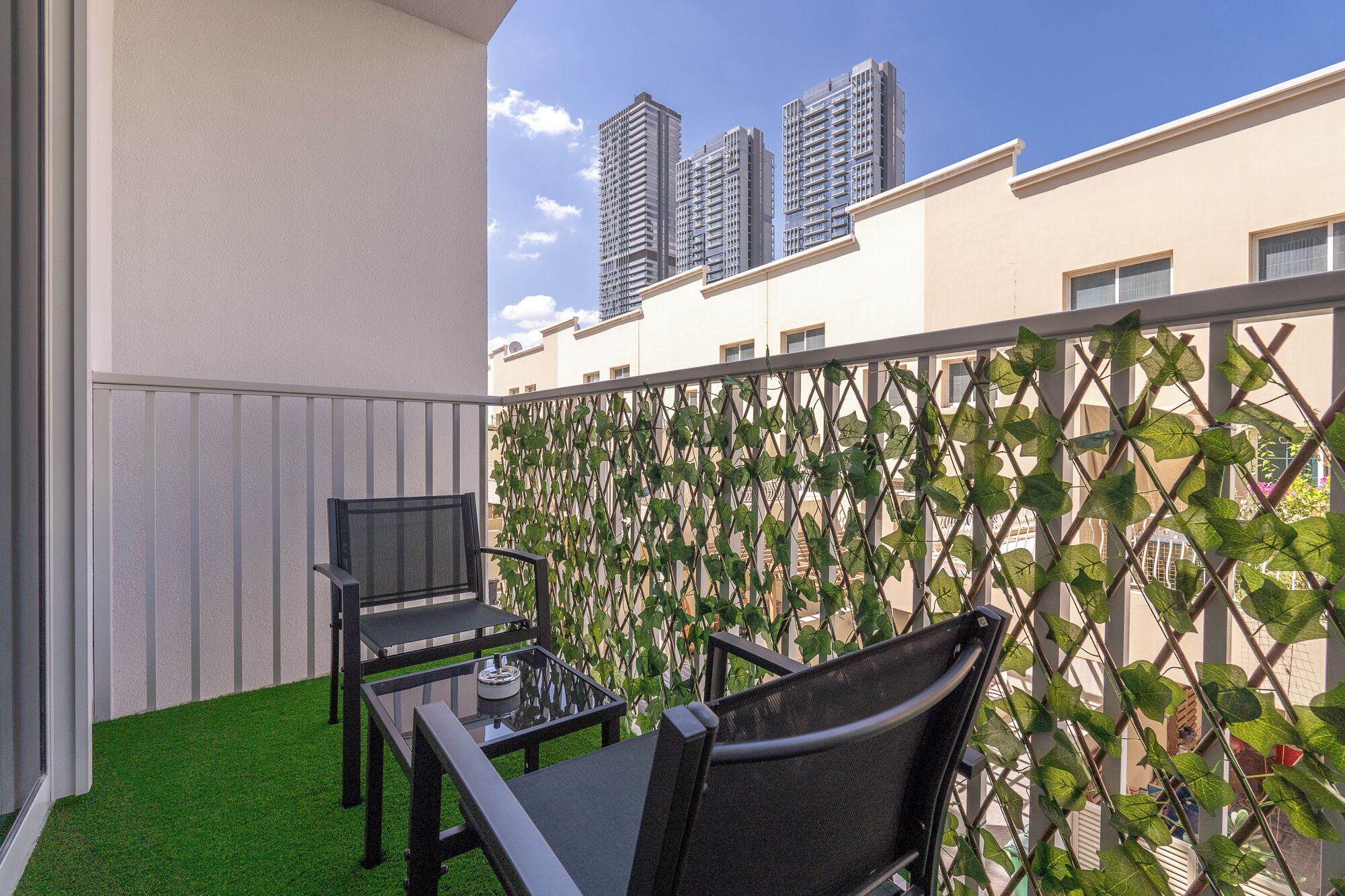 Ein Balkon mit Tisch und Stühlen, einem Belag aus grünem Kunstrasen und einer Rankgitter-Umrandung.