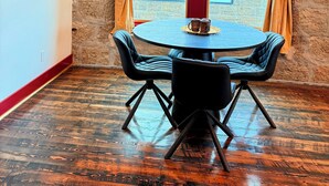 Een kamer met een stenen muur, een groot raam met gordijnen, een ronde tafel met stoelen en een muurschildering.